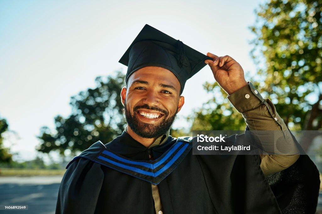 Portrait of smiling graduate in gown and hat standing alone on university campus at graduation ceremony. Excited, happy qualified postgrad graduating college for academic bachelor, masters and degree Graduation Stock Photo