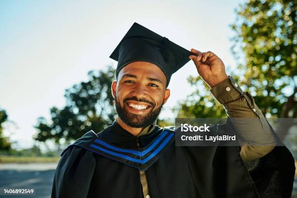 Portrait Of Smiling Graduate In Gown And Hat Standing Alone On University Campus At Graduation Ceremony Excited Happy Qualified Postgrad Graduating College For Academic Bachelor Masters And Degree Stock Photo - Download Image Now