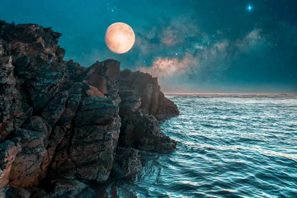 Photo of full moon over the cliff and ocean at night