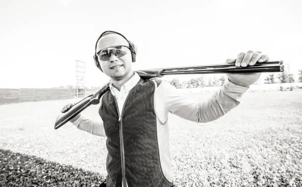 Photo of Portrait of adult smilling man in sunglasses, protective headphones and a rifle vest practicing fire weapon shooting.Portrait of adult man in sunglasses, protective headphones and a rifle vest practicing fire weapon shooting.