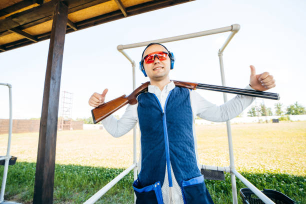 porträt eines erwachsenen milling-mannes mit sonnenbrille, schützenden kopfhörern und einer gewehrweste, die das schießen mit feuerwaffen übt. porträt eines erwachsenen mannes mit sonnenbrille, schützenden kopfhörern und einer gewehrweste, die das  - sport clipping path handgun pistol stock-fotos und bilder