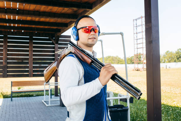 porträt eines erwachsenen mannes mit sonnenbrille, schützenden kopfhörern und einer gewehrweste, die das schießen mit feuerwaffen übt. porträt eines erwachsenen mannes mit sonnenbrille, schützenden kopfhörern und einer gewehrweste, die das schieße - sport clipping path handgun pistol stock-fotos und bilder