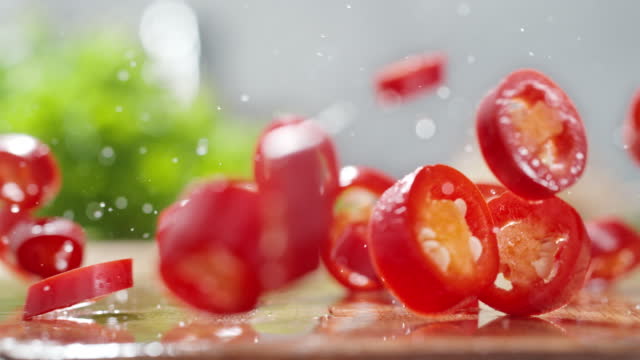 Throwing Red Chopped Chili Peppers onto the Wet Wooden Cutting Board in Slow Motion