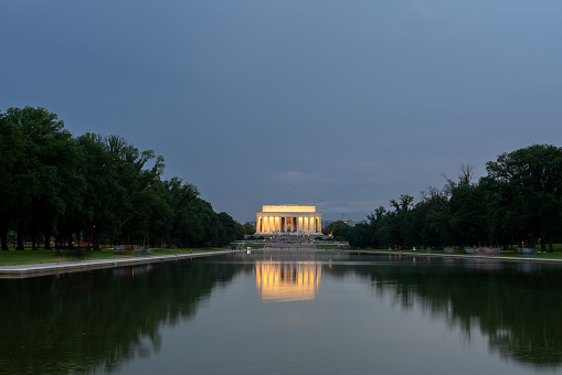 Lincoln Memorial Lit Up and Reflected on Water with Tourism on the Stairs and Cloudy Skies