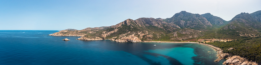 Panoramic view of a lone catamaran moored in a large rocky cove on the west coast of Corsica on the turquoise Mediterranean sea