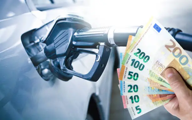 Gas prices. a man's hand shows banknotes in the background a car being refueled