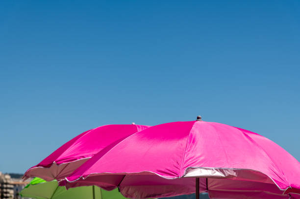 Colorful pink and green beach umbrellas against clear blue sky