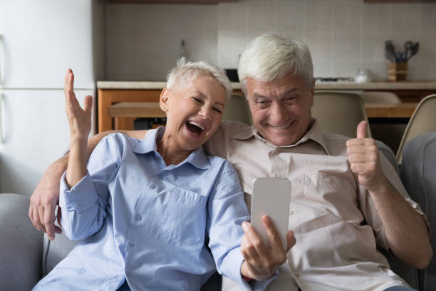 istock Overjoyed senior couple hug on sofa hold phone celebrate triumph 1406899714