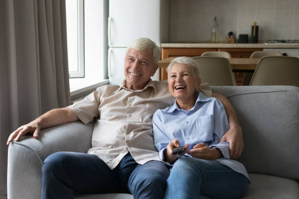 istock Laughing elderly spouses cuddle on couch watch tv movie comedy 1406899743