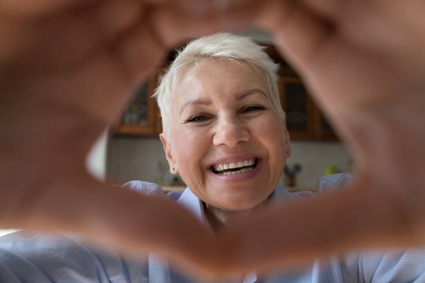 istock Happy smiling old lady look at camera in finger heart 1406899752