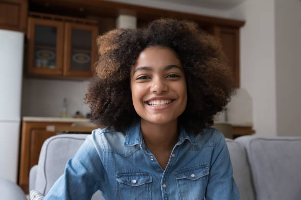 istock Cheerful young Black woman sitting on couch looking at webcam 1406899763