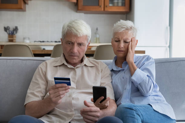 couple âgé choqué dépensant trop d’argent en ligne à l’aide d’un téléphone de carte de crédit - endettement photos et images de collection