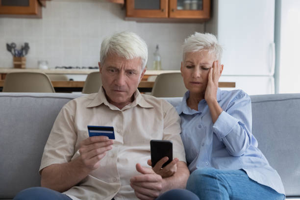 coppia di anziani scioccata che spende troppo soldi online usando il telefono con carta di credito - aging process old middle senior adult foto e immagini stock