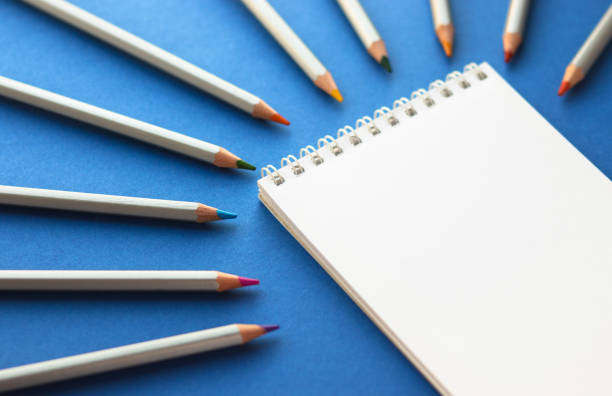 istock Blank notepad on spirals and colorful pencils on bright blue background. Sketchbook for drawing. Art and hobby concept. Copy space. 1406901406