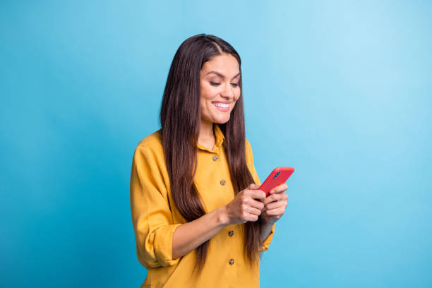 portrait of half turned pretty person toothy smile look phone have good mood isolated on blue color background - half smile imagens e fotografias de stock