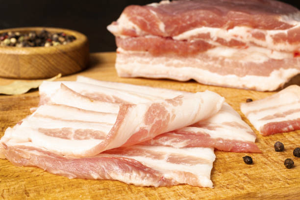 istock Raw bacon on wooden cutting board on brown background. 1406904033