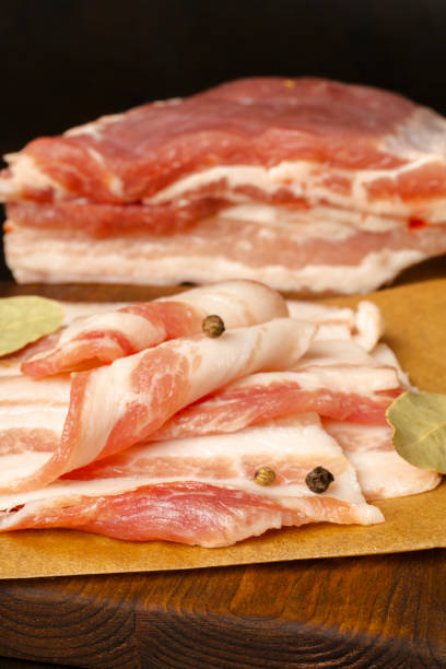 istock Raw bacon on wooden cutting board on brown background. 1406904656