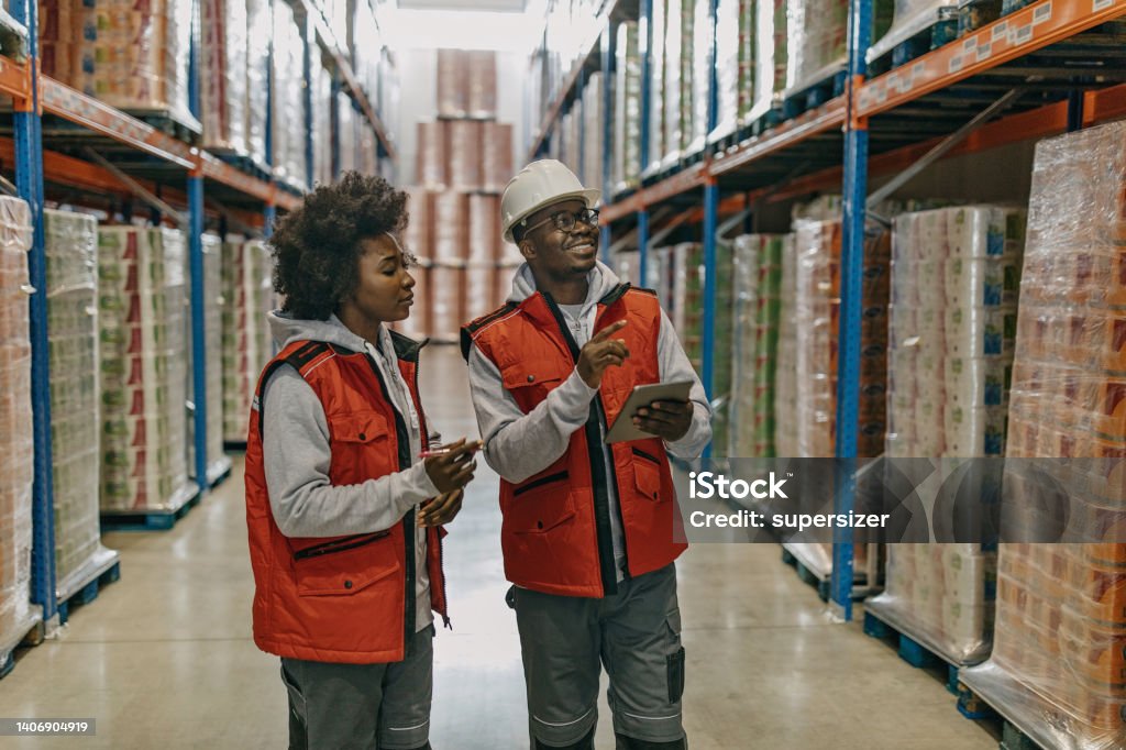 We need to ship these tomorrow A young African American man and woman are taking a look around a warehouse, wearing work clothes. 25-29 Years Stock Photo