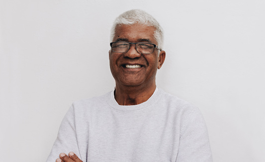 Happy senior man smiling at the camera while standing against a white background. Portrait of a cheerful mature man wearing eyeglasses.