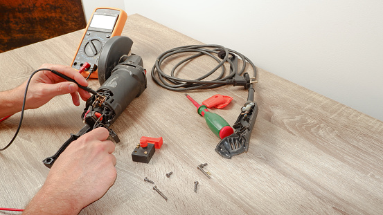 Power tool repair. A man repairs an angle grinder. Screwdriver, multimeter.