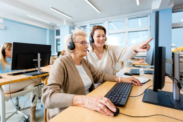 Manager explaining senior trainee using computer Smiling female manager explaining senior trainee using computer at desk in office middle age adult studying stock pictures, royalty-free photos & images
