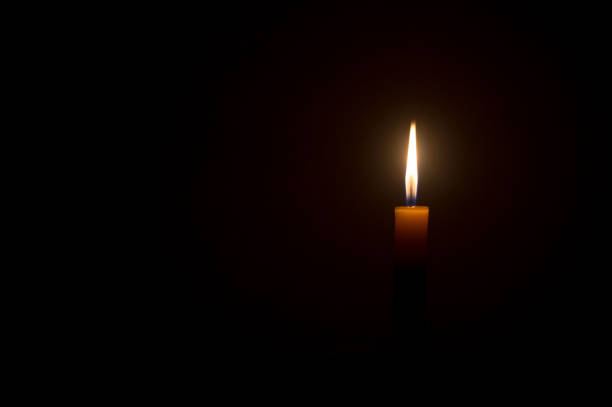 istock Single small yellow candle light glowing isolated on black or dark background on table in church or temple for Christmas, funeral or memorial service 1406910952