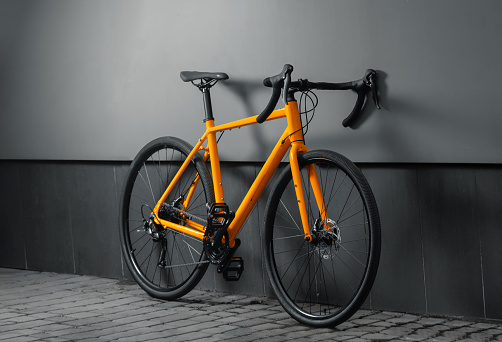 Gravel bicycle. Orange bike for cross country cycling on grey background.