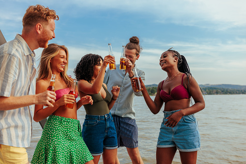 A cheerful group of multiethnic friends are partying on a river boat with beers and music