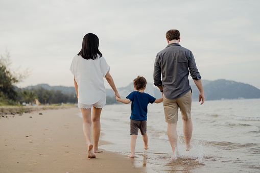 Happy family walk along the beach with their child on vacation.