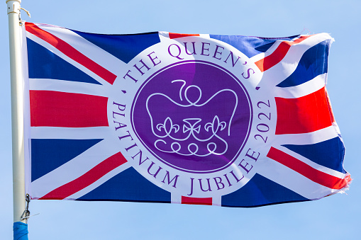 Norfolk, UK - April 8th 2022: A flag commemorating the Queens Platinum Jubilee 2022, flying over a clear blue sky.