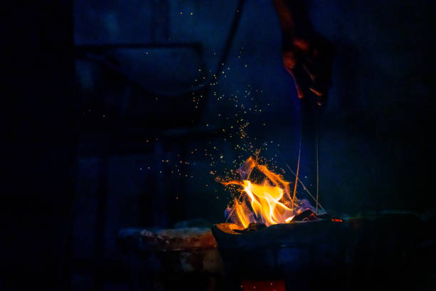 Hand adjust burning charcoal for cooking with flame and fire spark on dark background
