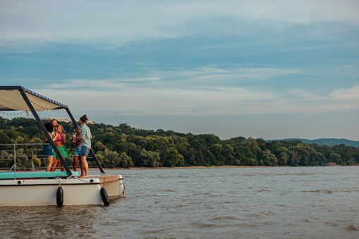 A river boat is on a river at a scenic landscape with a group of people having a casual day party at the boat.