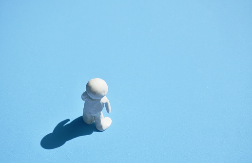 white clay man standing on sunlight with shadow on blue background