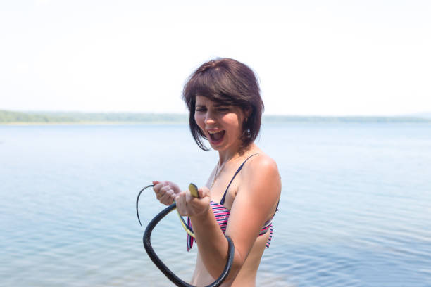 frightened woman screaming in fear while holding a snake in her hands, swimming on unverified beaches - unverified imagens e fotografias de stock