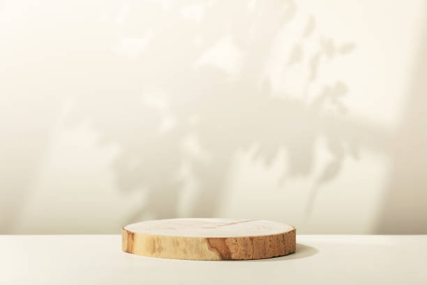화장품 모형을 위한 베이지 배경에 나뭇잎과 창 그림자가 있는 나무 조각 연단 스톡 사진