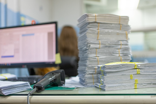 Stack of paper on desk waiting to convert data into computer with bar code reader.