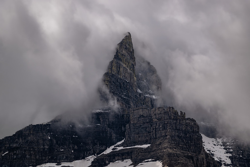 A prominent and sharp mountain peak juts into the clouds in Glacier National Park, Montana