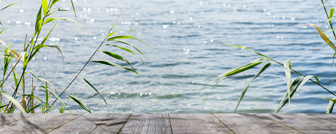 wooden dock lakeside in sunshine, blurred water with sun lights behind empty wooden planks for product presentation in idyllic water landscape, beautiful summertime background concept