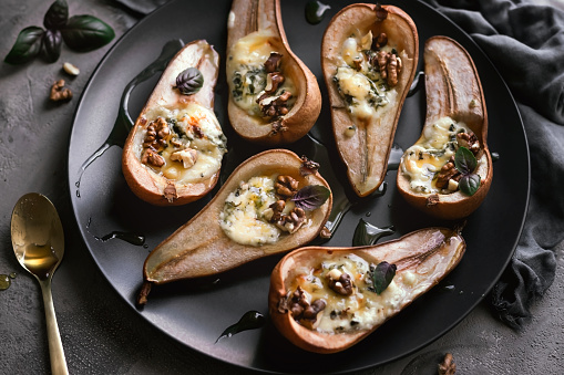 Pears baked with dorblu cheese, walnuts and honey are served on a plate.