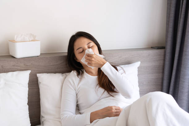 istock Sick young Asian woman feeling cold and has a high fever blowing nose while lying down on bed in the morning at home. Allergy, flu concept. 1406929414
