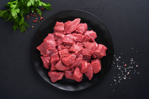 Raw chopped beef meat. Raw organic meat beef or lamb, spices, herbs on black plate on dark grey concrete background. Goulash. Raw uncooked meat. Meat with blood. Top view with copy space. stock photo