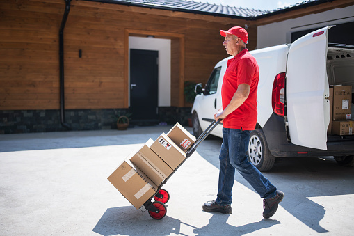 Delivery person delivering parcels with push cart to the door.