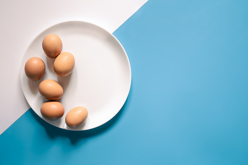 Flat lay, eggs on a white plate on a blue background, conceptual minimalism.