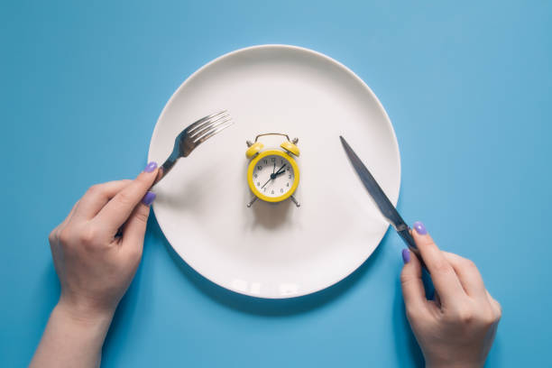 istock Hands holding knife and fork above alarm clock on a plate on blue background. 1406930574