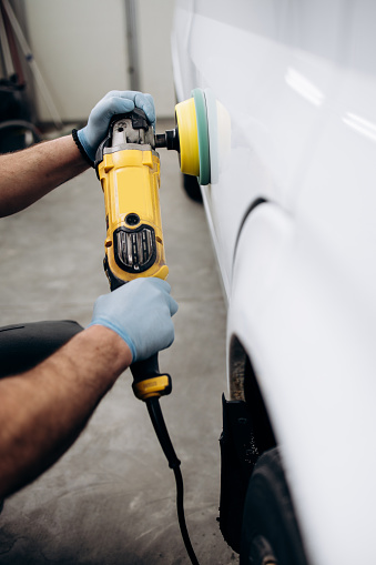 Car detailing - Hands with orbital polisher in auto repair shop. Selective focus.