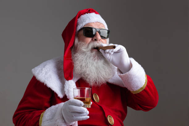 Santa Claus wearing sunglasses smoking a cigar and drinking whisk on dark background Santa Claus wearing sunglasses smoking a cigar and drinking whisk on dark background cigar photos stock pictures, royalty-free photos & images