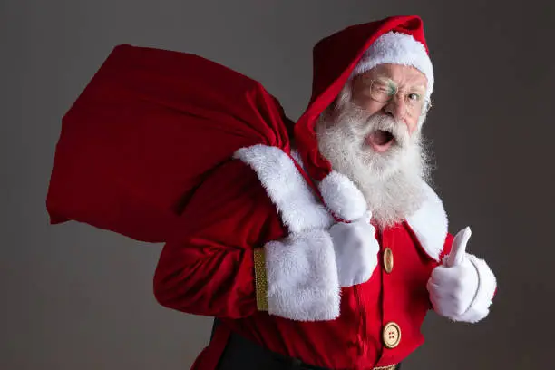 Photo of Santa Claus in eyeglasses is looking at camera and smiling, on gray background
