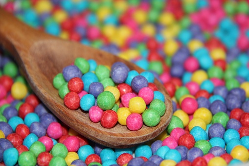 Small colored sugar balls in a wooden spoon with blurred background.