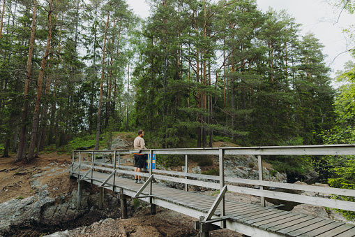 Young man walking at the wooden bridge inside the scenic green forest - admiring the beautiful Swedish nature