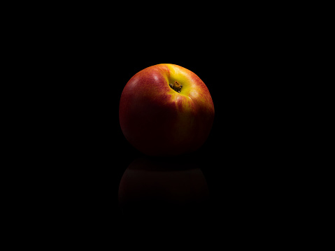 Nectarine with reflections on black background. Dark and moody photograph.